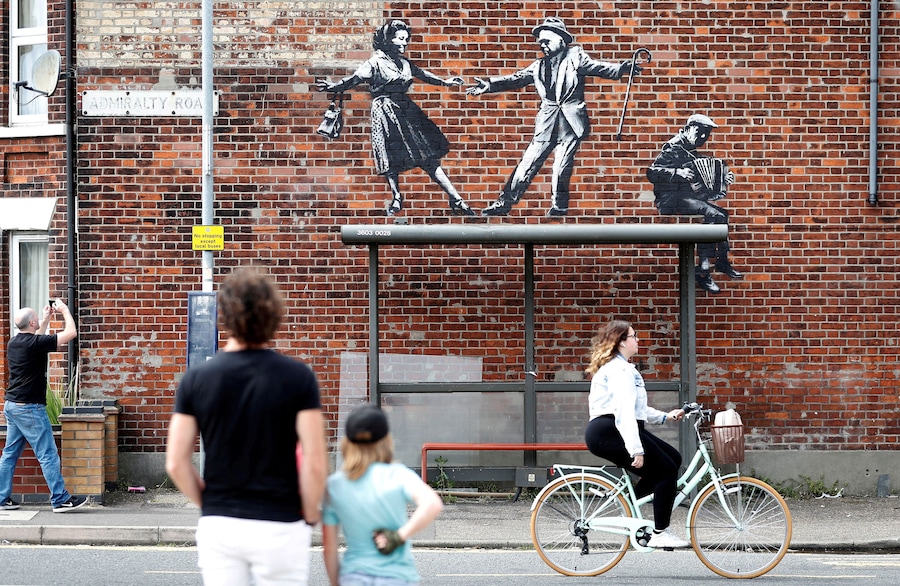 Alcuni passanti si fermano ad ammirare un'opera di Banksy a Great Yarmouth, in Gran Bretagna, l'8 agosto 2021. REUTERS/Peter Nicholls (REUTERS)