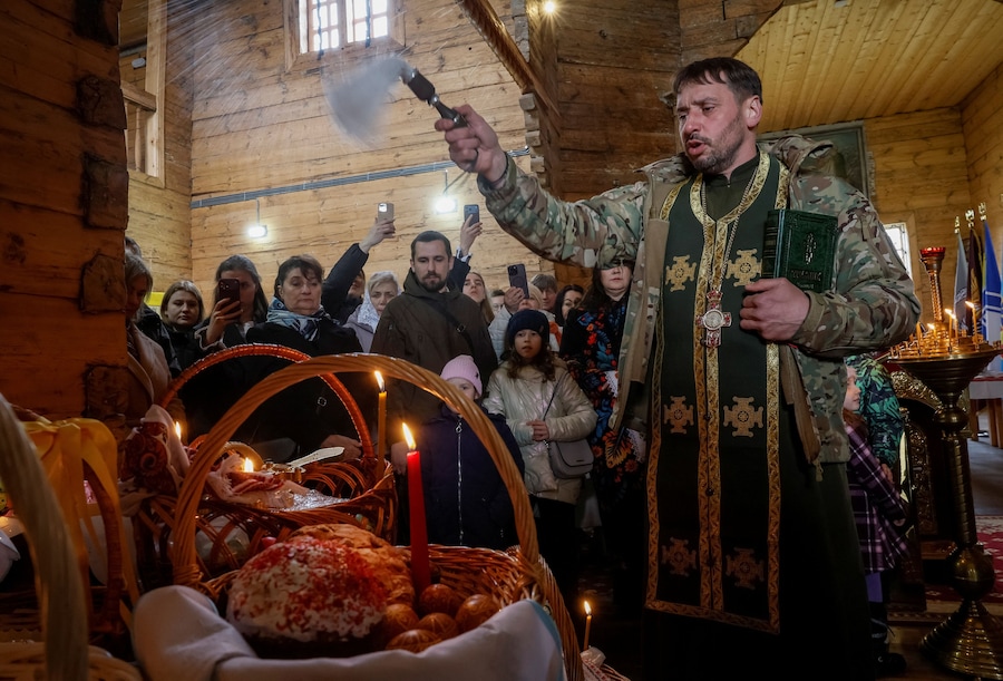 Un cappellano militare ucraino benedice spruzzando acqua santa sui dolci pasquali e sui cesti tradizionali dopo la funzione pasquale ortodossa, a seguito di una tregua di 32 ore dichiarata dalla Russia, nel contesto dell'attacco russo all'Ucraina, in una chiesa della guarnigione presso il Museo Nazionale di Architettura Popolare a Kiev, Ucraina, il 12 aprile 2026. REUTERS/Gleb Garanich (REUTERS)