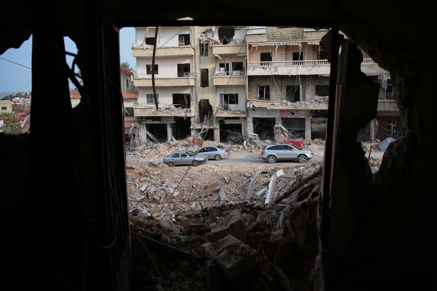 Gli abitanti del luogo passano in auto davanti al sito degli edifici distrutti da un raid aereo israeliano a Jibchit, nel Libano meridionale (APN)