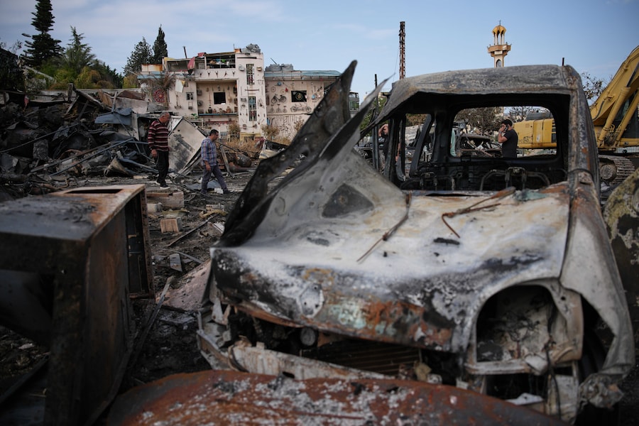 Gli abitanti del luogo camminano tra i veicoli bruciati in un raid aereo israeliano a Jibchit, nel sud del Libano (APN)