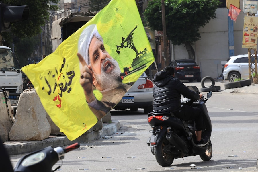 Una persona in scooter porta una bandiera con l’immagine del leader di Hezbollah Naim Qassem, mentre gli sfollati si dirigono verso le proprie case dopo l’entrata in vigore di un cessate il fuoco di 10 giorni tra Libano e Israele, nella periferia meridionale di Beirut, Libano (REUTERS)