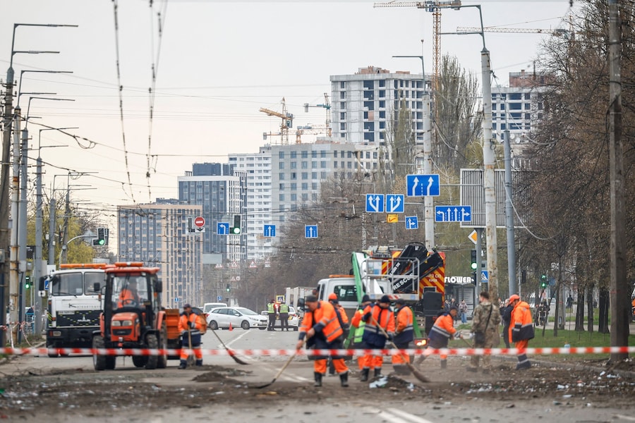 Operai ripuliscono una strada nei pressi di alcuni condomini danneggiati nel luogo colpito da un missile russo a Kiev. (REUTERS/Alina Smutko)