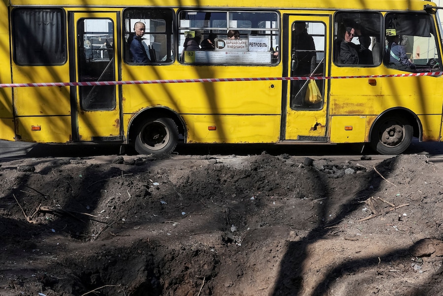 A Kiev alcune persone salgono su un autobus nei pressi di un cratere nel luogo in cui si è verificato un attacco russo con missili e droni, nell'ambito dell'offensiva russa contro l'Ucraina. (REUTERS/Anatolii Stepanov)
