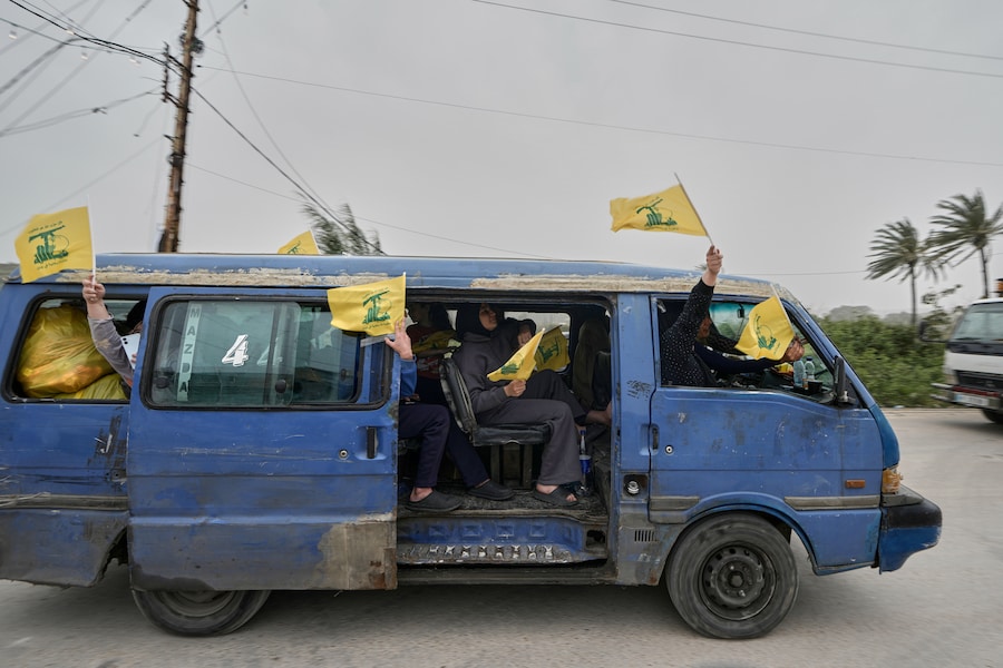 Alcuni sfollati seduti su un furgone sventolano bandiere di Hezbollah mentre tornano nei loro villaggi. (APN)