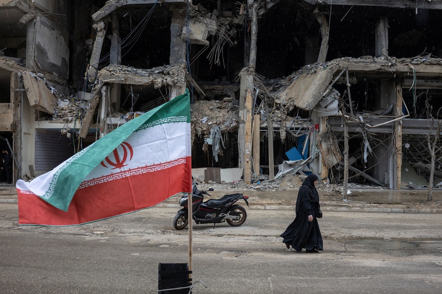 Una bandiera iraniana sventola mentre una donna cammina tra gli edifici danneggiati durante il cessate il fuoco di 10 giorni tra Libano e Israele, nella periferia meridionale di Beirut, Libano (REUTERS)