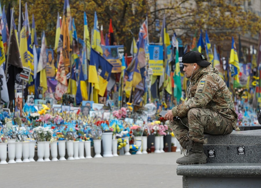 Un uomo in uniforme militare siede vicino a un memoriale improvvisato dedicato ai soldati ucraini caduti e ai volontari internazionali in Piazza dell’Indipendenza a Kiev, Ucraina (EPA)