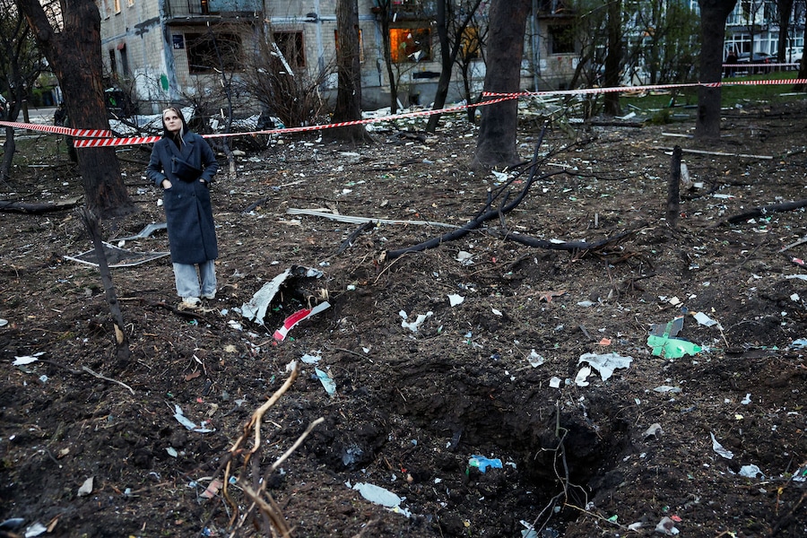 Una donna osserva la scena mentre si trova in una zona disseminata di detriti vicino al luogo colpito da un missile russo, a Kiev. (REUTERS/Alina Smutko)