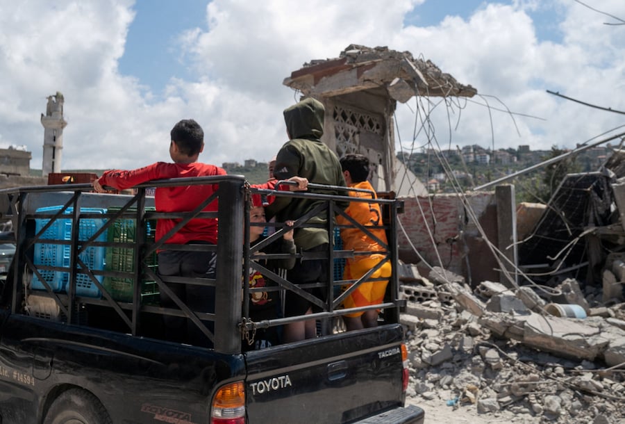 Dei bambini sono in piedi sul cassone di un pick-up mentre questo passa davanti agli edifici danneggiati da un attacco israeliano nel villaggio di Mansouri, nel sud del Libano. (REUTERS/Zohra Bensemra)