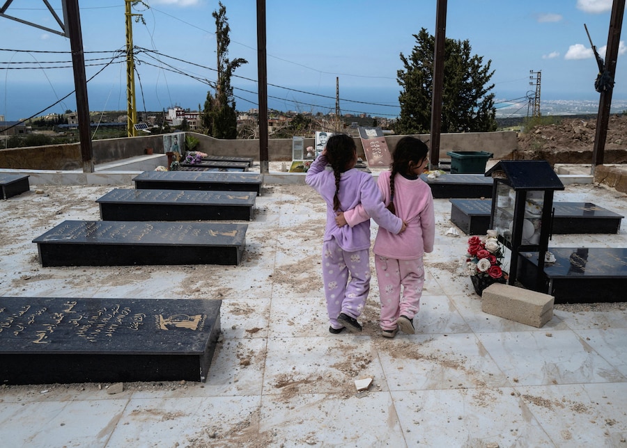 Due bambine, sfollate e poi rientrate durante i 10 giorni di cessate il fuoco, camminano vicino alle tombe dei combattenti di Hezbollah uccisi da un attacco israeliano mentre visitano il cimitero dove è sepolto il loro nonno, nel villaggio di Majdelzon, nel Libano meridionale. (REUTERS/Zohra Bensemra)