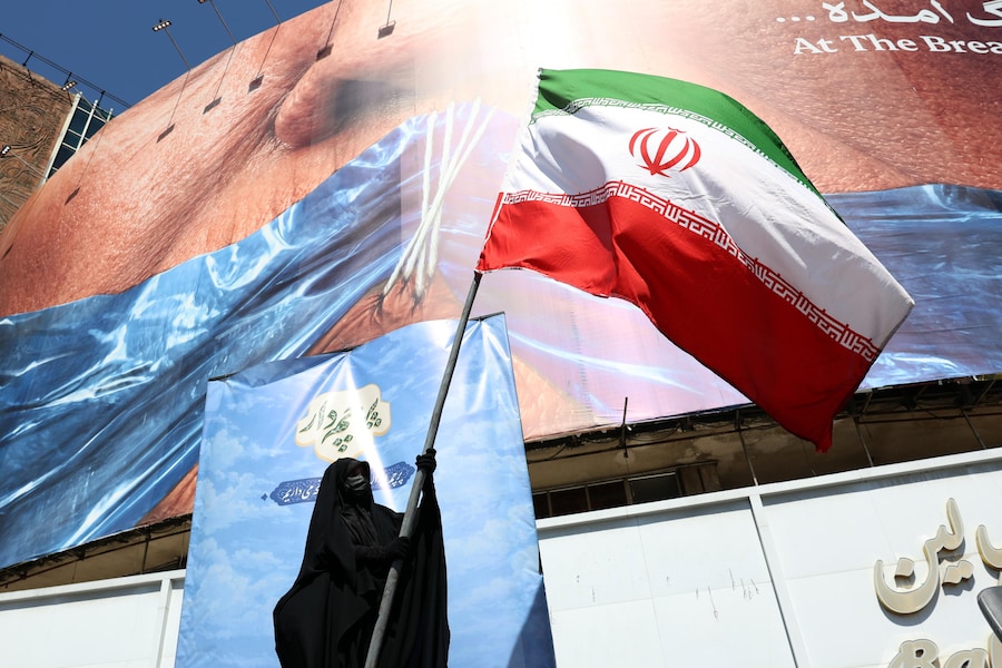 Una donna velata tiene in mano la bandiera nazionale iraniana davanti a un enorme cartellone pubblicitario anti-statunitense che fa riferimento al presidente degli Stati Uniti Donald Trump e allo Stretto di Hormuz, in piazza Valiasr a Teheran, Iran, l'11 maggio 2026. (EPA)