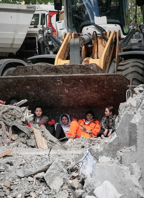 Alcuni scolari, con dei fiori in mano, sono seduti nella benna di un escavatore sul luogo dell'attacco missilistico russo che ha colpito un edificio residenziale a Kiev. (AP Photo/Efrem Lukatsky/APN)
