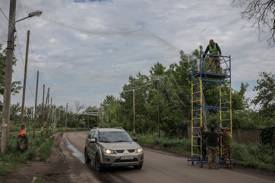 Alcuni operai e militari impegnati a installare reti anti-drone sopra una strada, nella regione di Donetsk, Ucraina. (REUTERS)