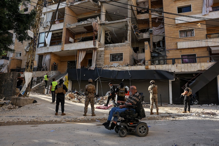 Un uomo in sedia a rotelle passa accanto al personale di emergenza che lavora sul luogo di un attacco israeliano nella periferia meridionale di Beirut, in Libano (REUTERS)