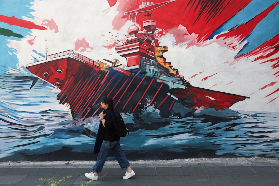 Una donna iraniana cammina accanto a un murale anti-USA in una strada di Teheran, Iran (via REUTERS)