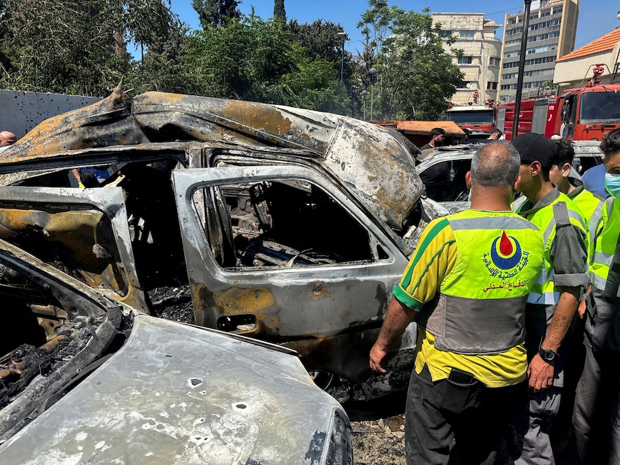 Operatori dei servizi di emergenza in piedi accanto a veicoli bruciati, in seguito a un attacco israeliano a Sidone, nel sud del Libano (REUTERS)