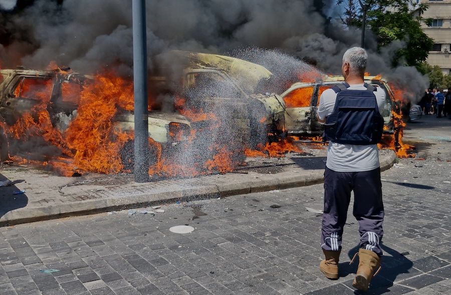 Un operatore della protezione civile spegne le auto in fiamme colpite da un raid aereo israeliano nella città portuale meridionale di Sidone, in Libano (APN)