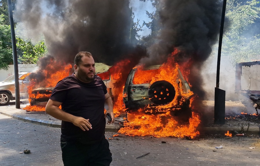 Un uomo corre davanti ad auto bruciate, colpite da un raid aereo israeliano nella città portuale meridionale di Sidone, in Libano (APN)