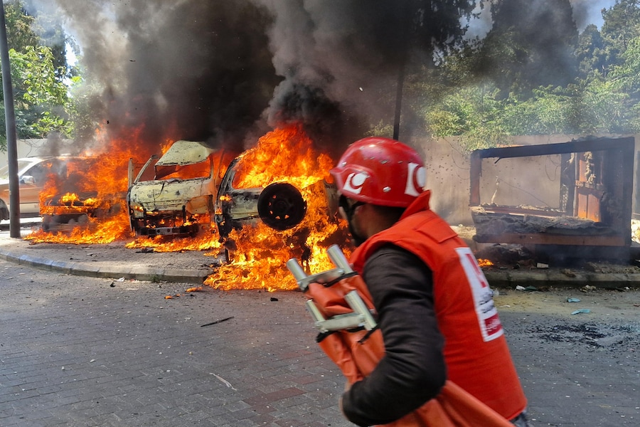 Un paramedico corre davanti ad auto bruciate, colpite da un raid aereo israeliano nella città portuale meridionale di Sidone, in Libano (APN)