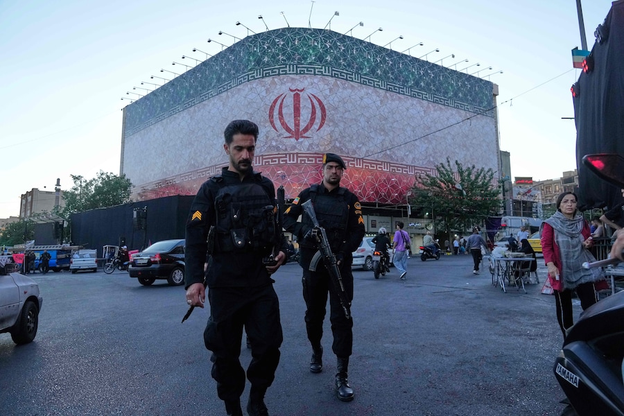 Poliziotti camminano davanti a un enorme striscione con la bandiera iraniana in Piazza della Rivoluzione Islamica a Teheran, Iran (APN)