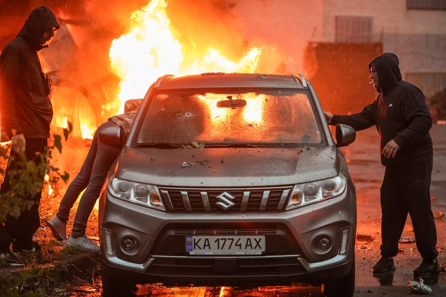 Residenti cercano di spostare un’auto dal luogo di un attacco missilistico e di un drone russo a Kiev, Ucraina (REUTERS)