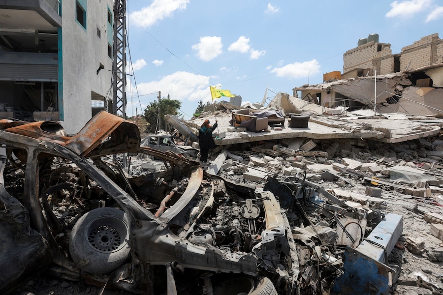 Una donna tiene in mano una bandiera di Hezbollah tra le macerie di edifici distrutti, a Deir Qanoun al-Nahr, nel distretto di Tiro, nel Libano meridionale. (REUTERS/Aziz Taher)