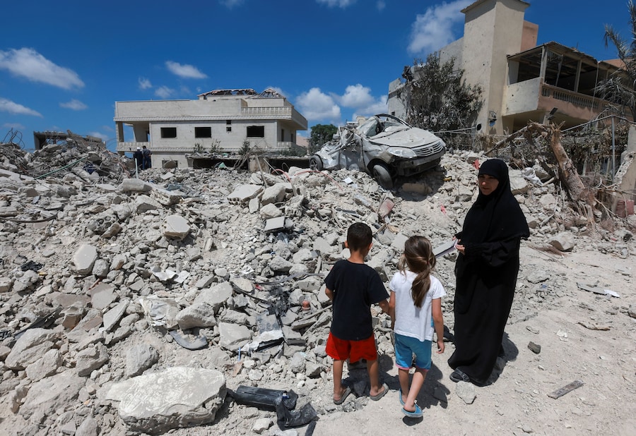 Una donna in compagnia di alcuni bambini accanto a cumuli di macerie provenienti da edifici distrutti a Deir Qanoun al-Nahr, nel distretto di Tiro, nel Libano meridionale. (REUTERS/Aziz Taher)