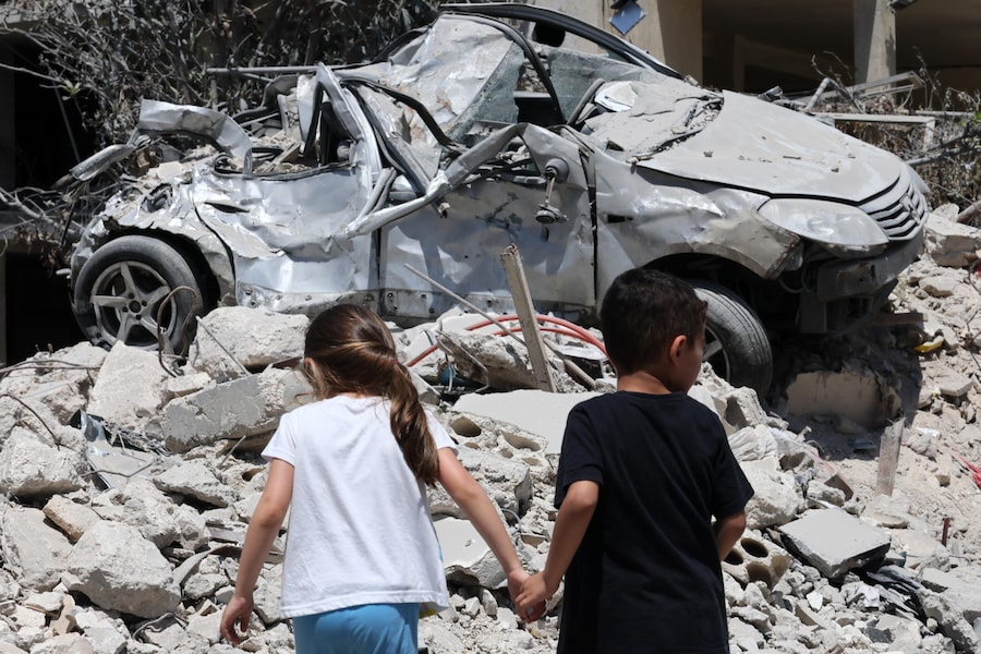 Dei bambini camminano accanto a un'auto danneggiata in seguito a un attacco israeliano nel villaggio di Maaroub, nel sud del Libano, dopo l'annuncio di un accordo quadro preliminare mediato da Stati Uniti e Iran per porre fine alle ostilità militari nella regione e revocare il blocco navale dello Stretto di Hormuz. (EPA/WAEL HAMZEH)