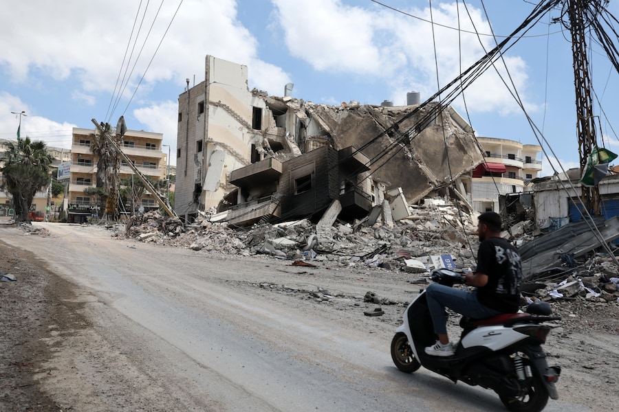 Un uomo passa in moto davanti a un edificio distrutto in seguito a un attacco israeliano nel villaggio di Kfar Reman, nel Libano meridionale. (EPA/WAEL HAMZEH)