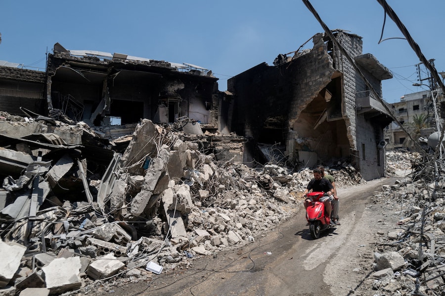 Uomini in motocicletta passano davanti a negozi ed edifici danneggiati dai raid israeliani a Nabatieh, Libano (REUTERS)