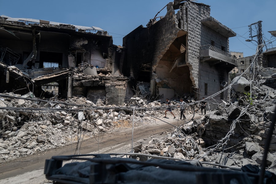 Uomini camminano davanti ad edifici danneggiati dai raid israeliani a Nabatieh, in Libano (REUTERS)