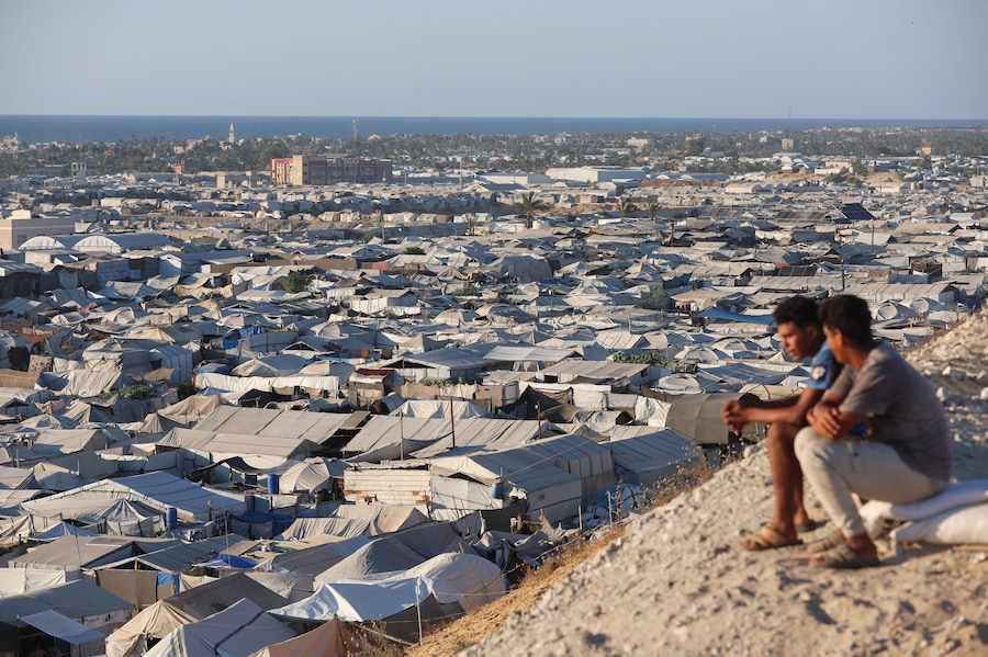 Alcuni palestinesi sono seduti a guardare un campo tendato che ospita sfollati, a Khan Younis, nella parte meridionale della Striscia di Gaza. (REUTERS/Ramadan Abed)