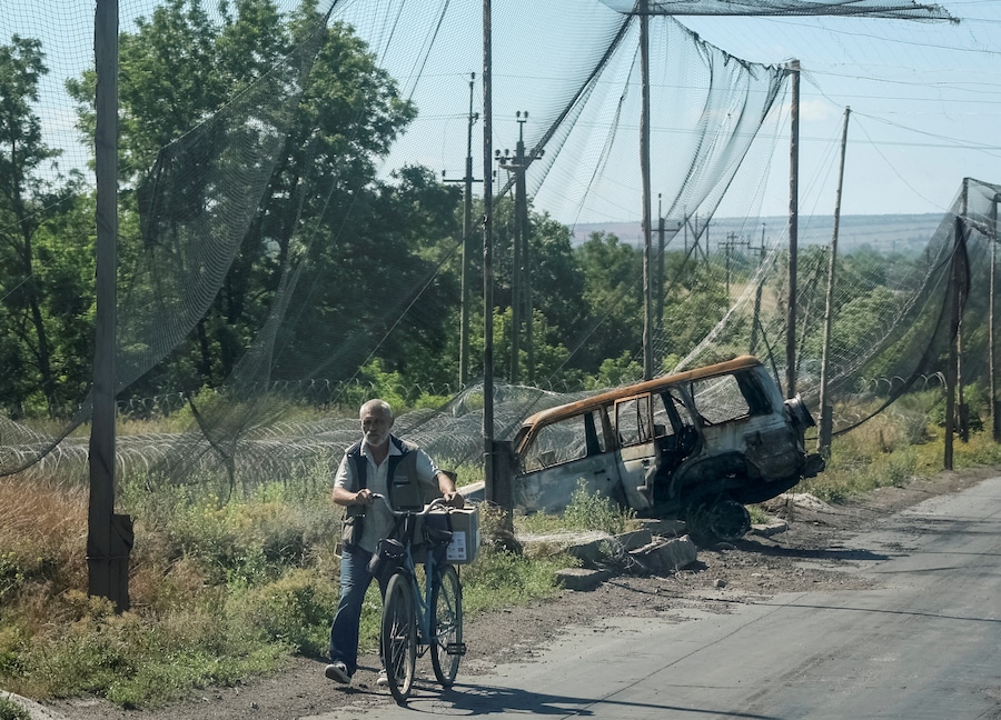 Un abitante spinge una bicicletta lungo una strada ricoperta da reti anti-drone e con filo spinato installato nelle vicinanze, mentre la Russia attacca l’Ucraina, nella città di Druzhkivka, in prima linea nella regione di Donetsk. (REUTERS/Anatolii Stepanov)