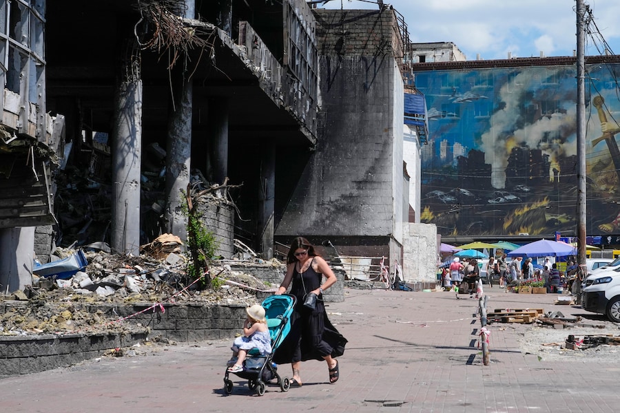 Una madre spinge un passeggino davanti a un edificio danneggiato, ricoperto dai murales di artisti di strada, e a un grande mercato cittadino recentemente distrutto dai missili russi a Kiev. (Foto AP/Efrem Lukatsky/Associated Press/ LaPresse/APS)