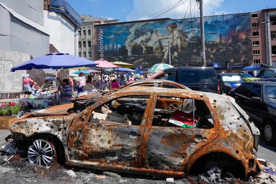 La gente fa la spesa in un mercato all’aperto improvvisato, con auto bruciate in primo piano, circondata da edifici danneggiati ricoperti dai murales di artisti di strada, nei pressi di un grande mercato cittadino recentemente distrutto dai missili russi a Kiev. (Foto AP/Efrem Lukatsky/Associated Press/ LaPresse/APS)