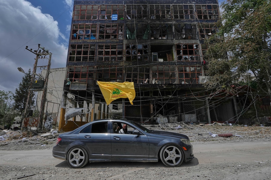Un uomo con una bandiera di Hezbollah passa in auto davanti a un edificio colpito nella città di Nabatiyeh, nel sud del Libano. (APN)