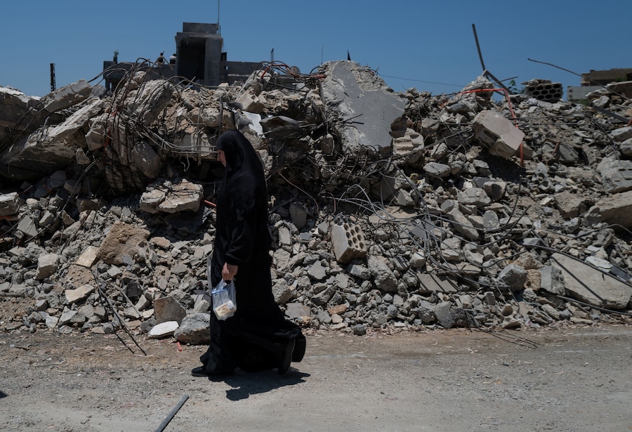 Una donna passa davanti alla casa del vicino, distrutta da un attacco aereo israeliano, dopo aver fatto ritorno a Maaroub, comune del distretto di Tiro, nel Libano meridionale (REUTERS)