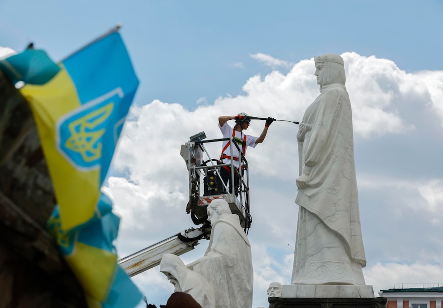Un operaio pulisce il monumento alla principessa Olga accanto a una mostra di mezzi militari russi distrutti in piazza Mykhailivska a Kiev, in Ucraina. (EPA)