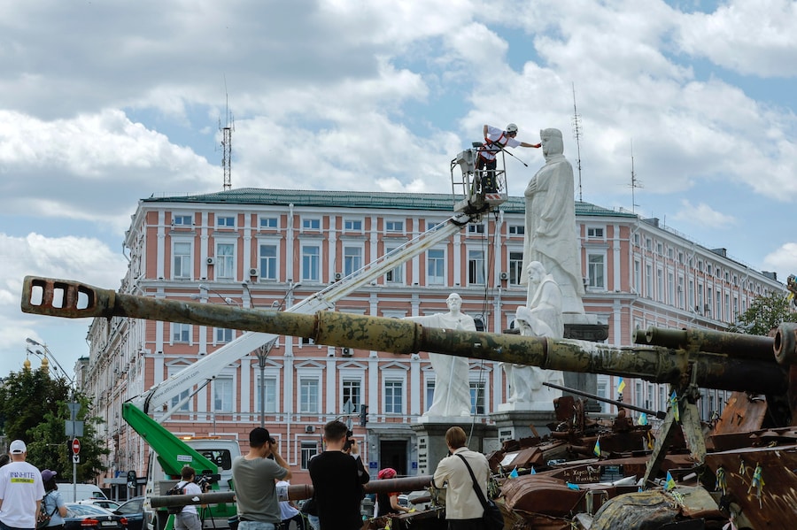 Un operaio pulisce il monumento alla principessa Olga accanto a una mostra di mezzi militari russi distrutti in piazza Mykhailivska a Kiev, in Ucraina. (EPA)