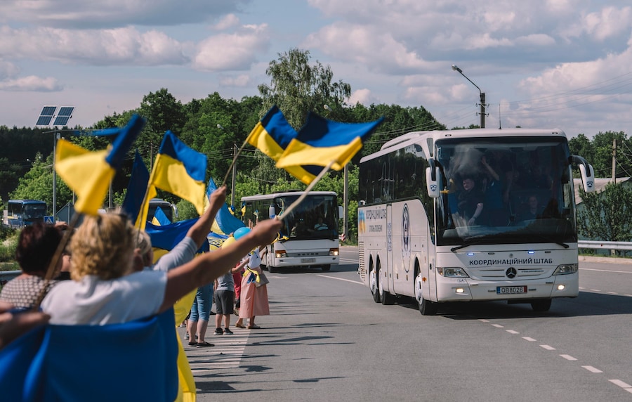 Una folla di sostenitori sventola bandiere nazionali per dare il benvenuto agli autobus che trasportano i prigionieri di guerra ucraini rimpatriati a seguito di uno scambio di prigionieri avvenuto in una località segreta in Ucraina, il 26 giugno 2026. (EPA)