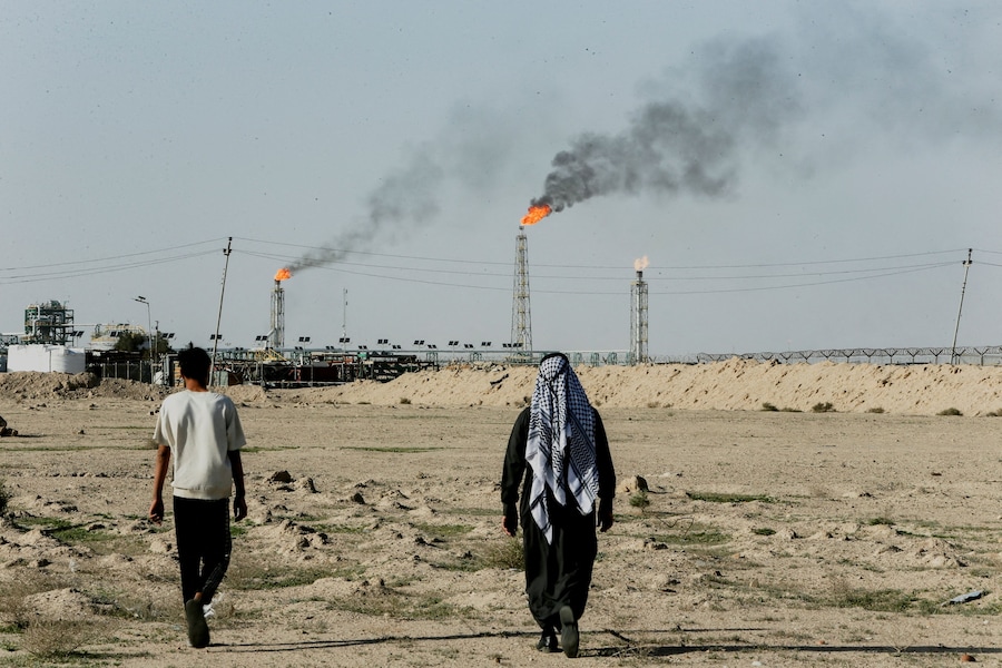 Persone che camminano nei pressi dei terreni agricoli vicino al giacimento petrolifero di Zubair mentre in lontananza si levano le fiamme delle torce a gas, a Zubair Mishrif, Bassora, Iraq. (REUTERS)