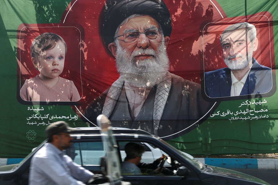 Le persone passano in auto davanti a uno striscione con l’immagine del defunto leader supremo iraniano, l’ayatollah Ali Khamenei, in vista della cerimonia di addio, a Teheran, in Iran. (via REUTERS)