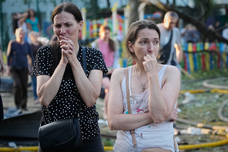 La gente reagisce sul luogo di un attacco missilistico russo che ha colpito un edificio residenziale a Kiev. (APN)