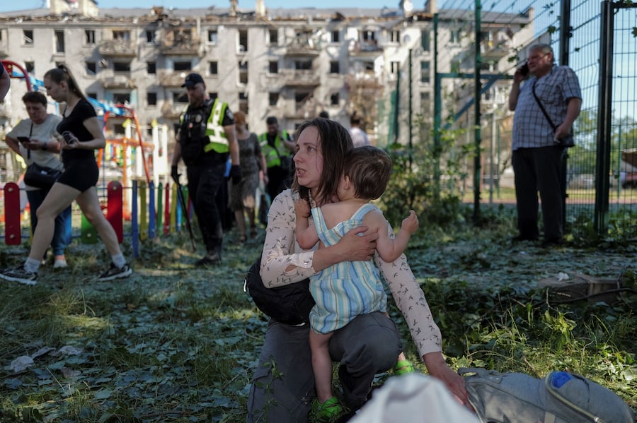 Una donna tiene in braccio un bambino vicino a un condominio danneggiato da un attacco russo con missili e droni a Kiev (REUTERS)