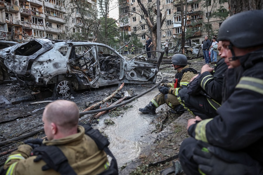 Alcuni vigili del fuoco si concedono una pausa mentre lavorano sul luogo colpito da missili e droni russi a Kiev (REUTERS)