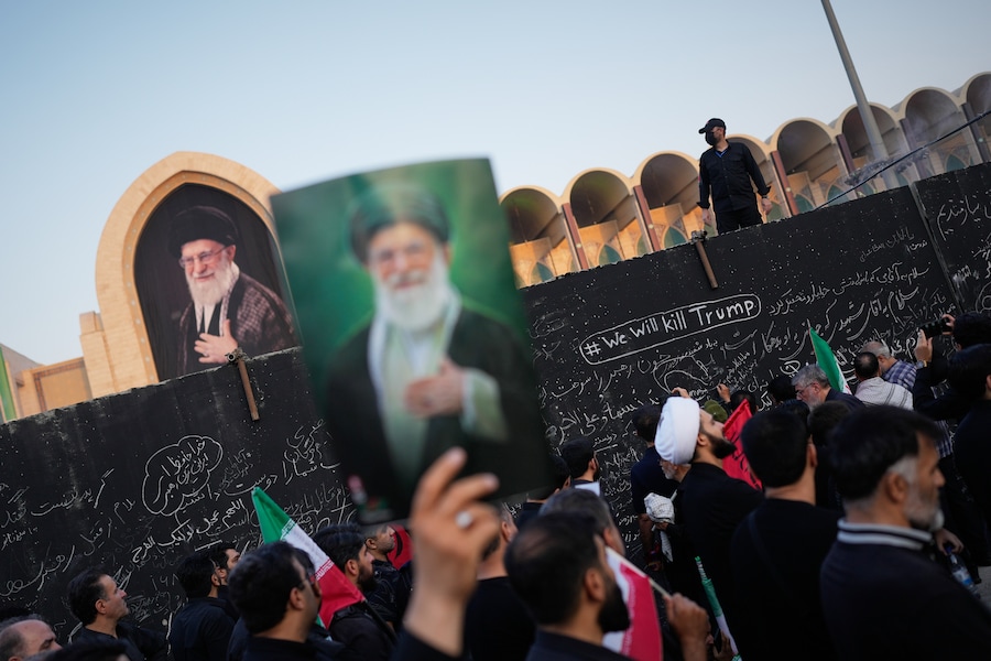 Un partecipante al funerale tiene in mano un ritratto del defunto leader supremo iraniano, l’ayatollah Ali Khamenei, mentre passa davanti a un muro su cui sono scritti diversi messaggi, tra cui uno in inglese che recita “Uccideremo Trump”. Teheran, Iran. (APN)