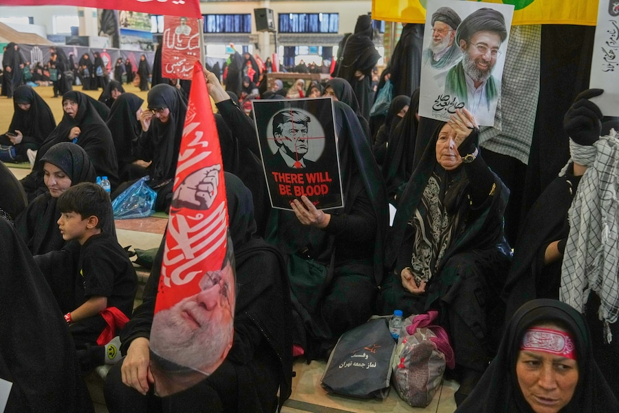 Una donna tiene in mano un manifesto che raffigura il presidente degli Stati Uniti Donald Trump nel mirino di un fucile, con la scritta in inglese "There Will Be Blood”, mentre un’altra donna tiene in mano un ritratto del defunto Leader Supremo Ali Khamenei e di suo figlio, l’attuale Leader Supremo Mojtaba Khamenei, durante la commemorazione del defunto leader presso la Grande Moschea Imam Khomeini Mosalla a Teheran, in Iran, martedì 14 luglio 2026. (APS)