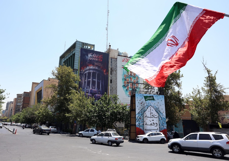 Alcuni iraniani transitano davanti a un cartellone anti-USA esposto a Piazza Palestina a Teheran (Iran); il manifesto raffigura il presidente statunitense Donald Trump e la sua famiglia sopra bare avvolte nella bandiera americana, accompagnati dalla scritta in persiano “Sangue per sangue” (EPA)
