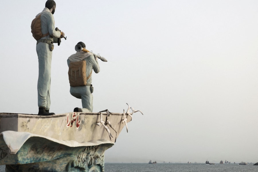 Una statua raffigurante militari iraniani si erge mentre, in primo piano, sono visibili alcune imbarcazioni nello Stretto di Hormuz, nei pressi della spiaggia di Bandar Abbas, in Iran. (Majid Asgaripour/WANA (West Asia News Agency) via REUTERS)