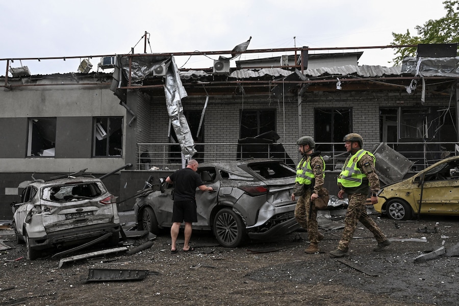 Un residente controlla la propria auto mentre alcuni membri della Guardia Nazionale passano davanti a un centro medico danneggiato durante un attacco aereo russo, nel contesto dell'offensiva russa contro l'Ucraina, a Zaporizhzhia. (REUTERS)
