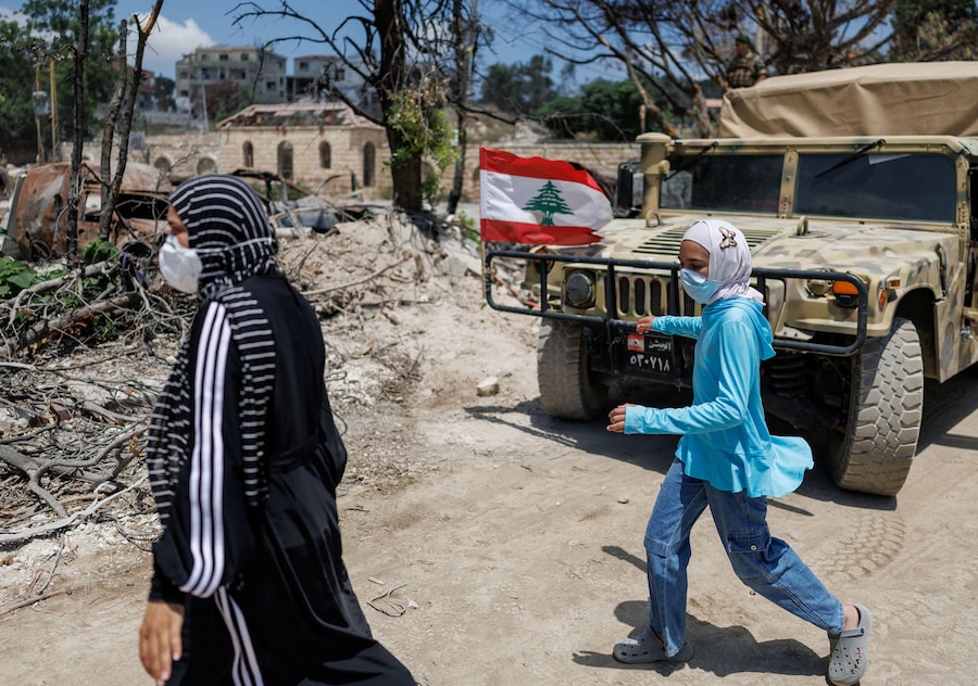 Due residenti passano accanto a un veicolo dell’esercito libanese dopo aver fatto ritorno a Zawtar al-Gharbiyeh, un villaggio nel sud del Libano (REUTERS)